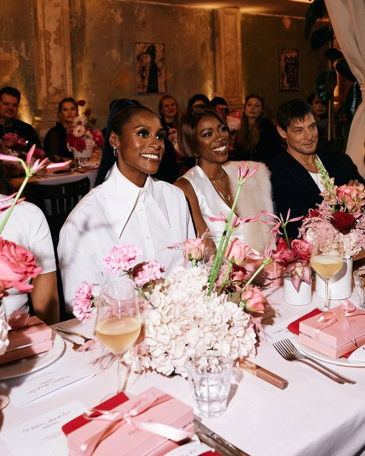 Guests smiling at a long dinner table decorated with pink flowers